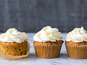 Three Carrot Cake Cupcakes topped with cream cheese frosting, one of them is partially unwrapped