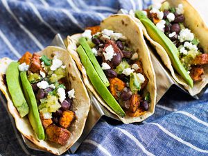 a row of Sweet Potato Black Bean Tacos topped with avocado, cotija cheese, and salsa verde