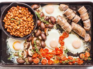 Full English Breakfast on a Sheet Pan -- a pot of beans, cracked eggs, sausages, potatoes, and tomatoes