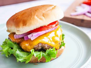 Grilled burger on a plate with cheese, onions, and tomatoes