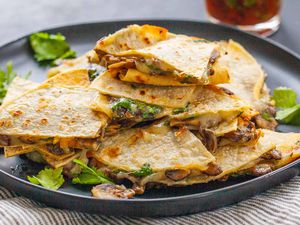 Vegetarian Quesadilla Recipe -close up of cheese and mushroom quesadillas stacked on top of each other with a jar of red salsa in the background.