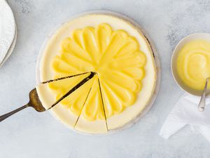 Lemon Curd Cheesecake - whole cheese cake with lemon curd on top and someone is about to take a slice out of it