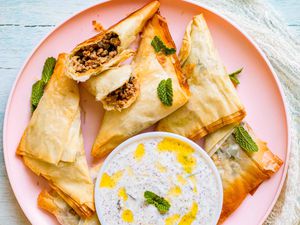 Easy Baked Indian Chicken Tikki Masala Samosa folded into a triangle with Mint Yogurt Dip on a pink plate with one samosa broken open.