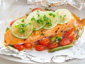 Roast salmon filet on foil with roast grape tomatoes, chopped cilantro and thinkly sliced lime on top.