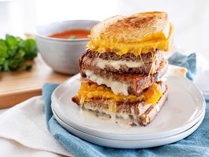 Grilled cheese sandwiches cut in half and stacked ontop of each other. Alternating with orange and white cheese with a bowl of tomato soup in the background.