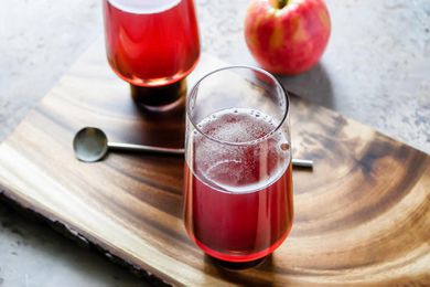 Hard Cider and Pomegranate Mimosa on a wooden board with an apple, stir spoon and second glass behind it.