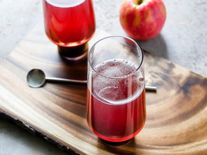 Hard Cider and Pomegranate Mimosa on a wooden board with an apple, stir spoon and second glass behind it.