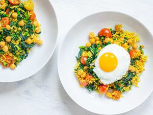 Overhead view of vegetable fried rice with turmeric with a fried egg on top and a fork in the bowl. A second bowl is to the left.