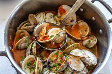Overhead view of steamed clams with chorizo in a large stockpot. A ladle is resting on top and is full of clams.