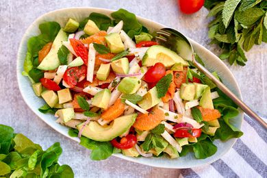 Overhead view of a summer citrus and avocado salad in a serving bowl. Mint and lettuce are also in the bowl.