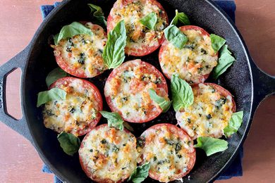 Overhead view of a cast iron skillet with vegetarian stuffed tomatoes with basil leaves scattered over top.