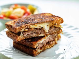 The best patty melt sliced in half and stacked on top of each other. The sandwich is crispy with melted cheese, caramelized onions and beef patties visible.