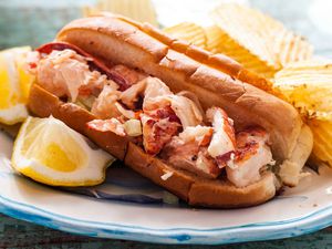 Plate of the best lobster roll recipe served with a side of chips and a lemon wedge.