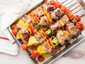 A quarter sheet pan has pork kebabs with grilled pineapple stacked on it.