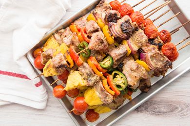 A quarter sheet pan has pork kebabs with grilled pineapple stacked on it.