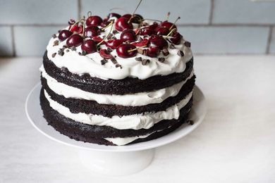 Side view of a Cherry Chocolate Cake with Whipped Cream on a white cake stand.