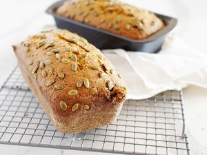 A loaf of Moist Pumpkin Bread cooling on a rack with a second loaf in the pan behind it.