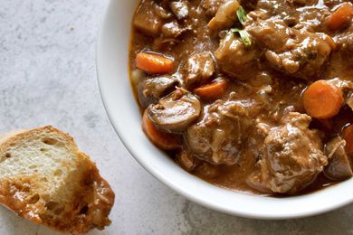 A slice of bread dipped into a bowl of Slow Cooker Beef Stew with Mushrooms, Onions and Carrots and set to the side.