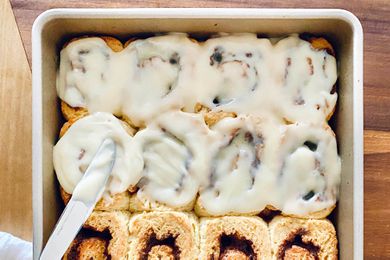 A pan of easy gluten free cinnamon rolls being topped with icing.