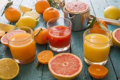 Glasses of orange juice, grapefruit juice and multivitamin juice, juice squeezer and fruits on wood