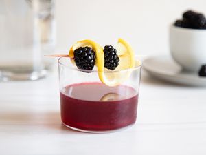Blackberry cosmopolitan cocktail in a tumbler garnished with blackberries and a lemon twist.