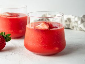 Two blender margaritas in wide glasses garnished with strawberries.
