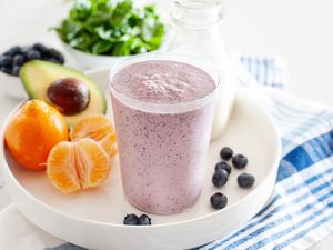 Blueberry breakfast smoothie on a tray along with fresh fruit and vegetables.