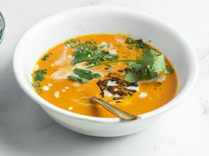 A bowl of blended coconut and carrot soup with savory cumin oil on a white background.