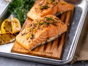 Cedar Plank Salmon on a Grilling Plank Next to Herbs and Grilled Lemon Wedges