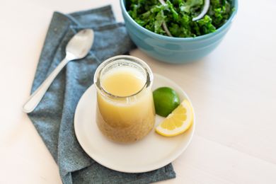 Creamy lemon and lime dressing in a glass jar set on a plate with a lemon and lime next to it.