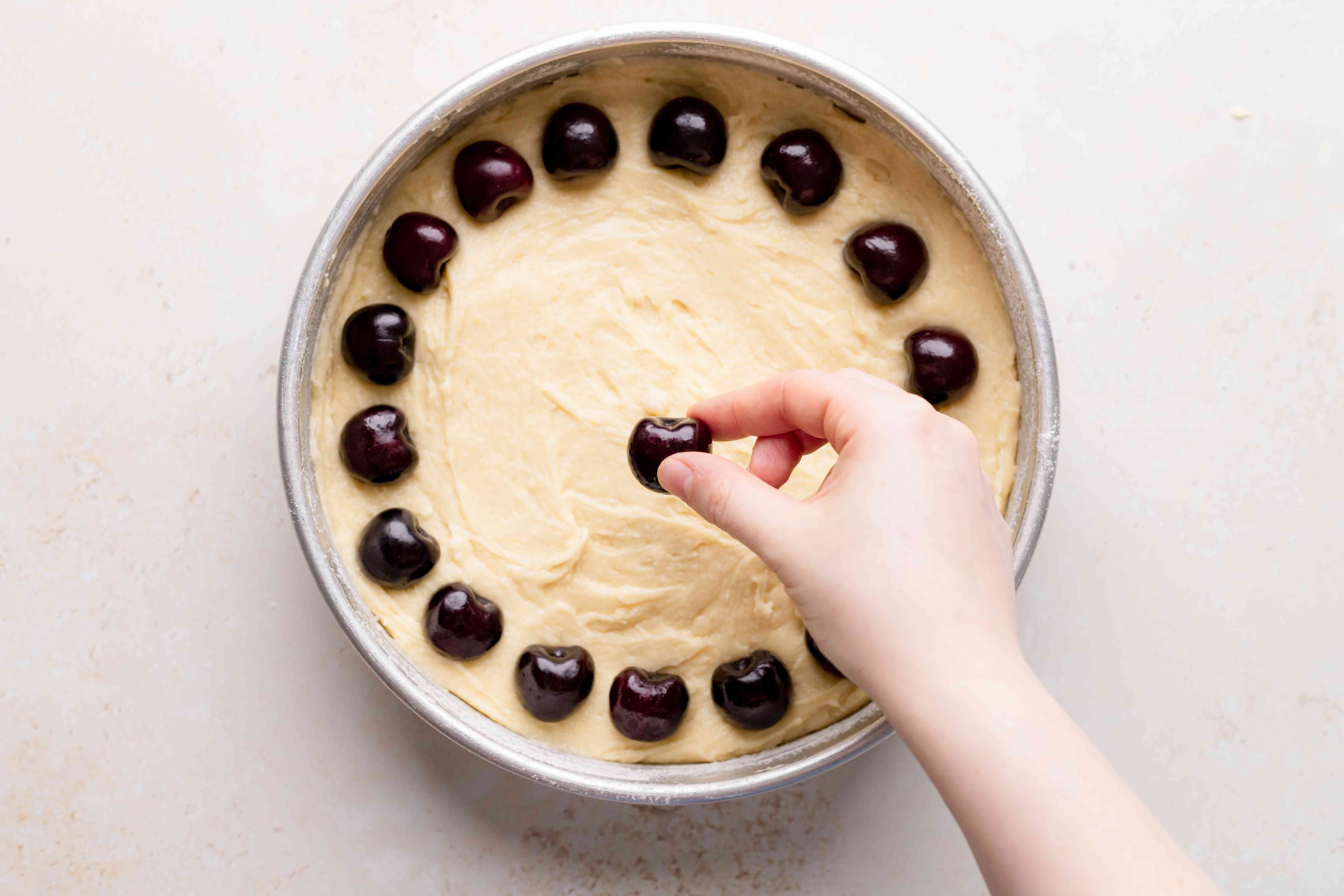 Placing fresh cherries on the batter of a cake to make a cherry cake from scratch.