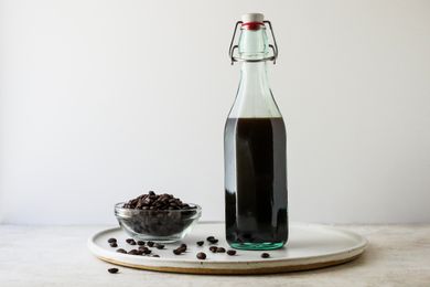 Side view of DIY Coffee Liqueur in a swing top bottle next to a small bowl of coffee beans.