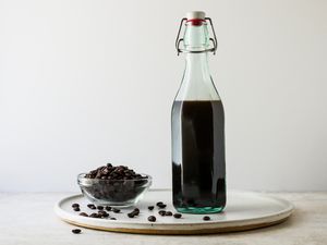 Side view of DIY Coffee Liqueur in a swing top bottle next to a small bowl of coffee beans.