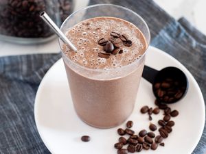 Creamy mocha coffee smoothie with a straw and set on a white plate with coffee beans next to it