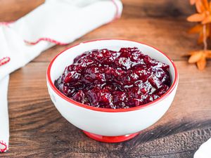 A bowl of cranberry sauce on a table with a spoon.