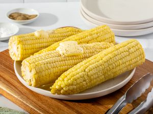 A plate of microwave corn on the cob set on a cutting board and topped with butter.