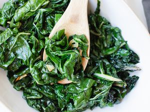 Wooden spoon scooping up cooked spinach recipe.