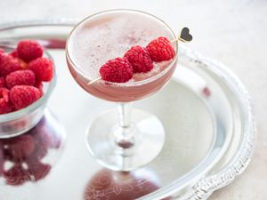 French Martini in a Glass Garnished with Raspberries on a Tray with a Bowl of Raspberries