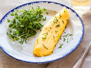 French Omelette with Greens on Plate Next to Fork and Glass