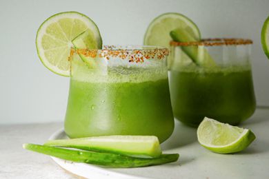 Two glasses of pitcher cucumber margaritas garnished with lime and cucumber.