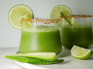 Two glasses of pitcher cucumber margaritas garnished with lime and cucumber.