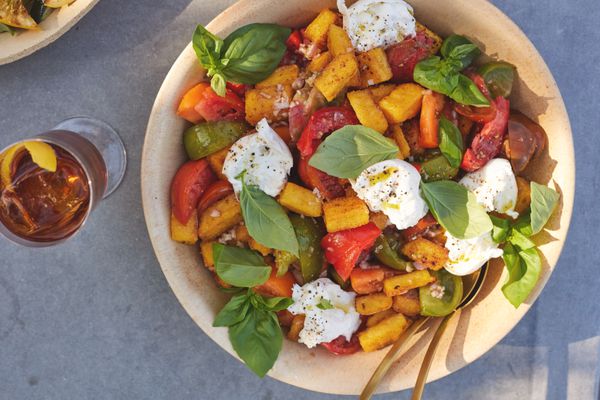 Bowl of Fried Polenta Panzanella with Tomato, Basil, and Burrata with a Drink on a Table
