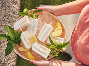 Someone Holding a Bowl of Limoncello Yogurt Pops on Ice Surrounded by Leaves and Lemons over Grass