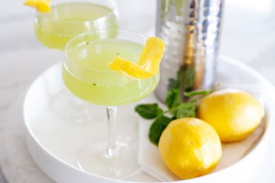 Two Gin Cucumber Cocktails on a white tray with lemons and a cocktail shaker.