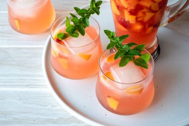 Two Glasses of Ginger Peach Rum Punch Garnished with Mint Next to a Pitcher
