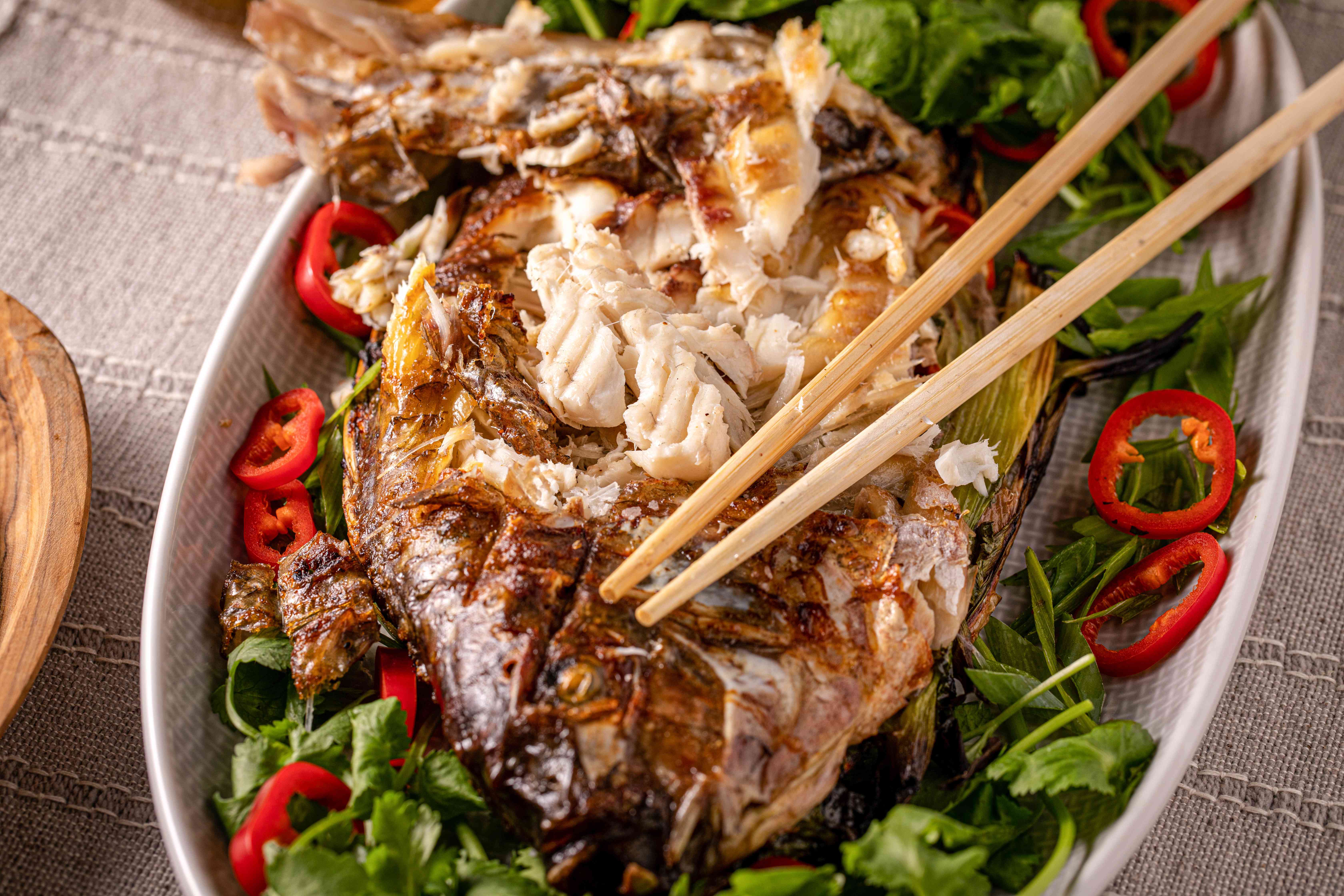 Wooden skewers flaking grilled whole fish stuffed with herbs and chilies