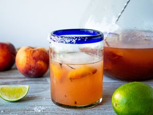 Grilled peach margarita on a table with limes and peaches.