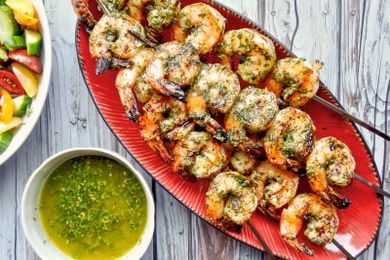 Skewers of Grilled shrimp with chermoula sauce on a red serving platter.