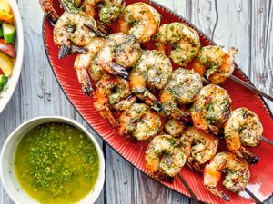 Skewers of Grilled shrimp with chermoula sauce on a red serving platter.
