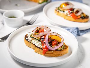 A white plate with zucchini, pepper, and onion tartines with goat cheese